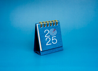Happy new year 2025 background. 2025 year numbers with target icon on blue small desk calendar...