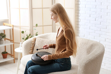 Beautiful young woman with sticks playing glucophone on sofa at home