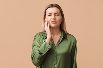 Young woman suffering from toothache on beige background