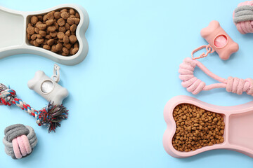 Bone shaped bowls with dry food and chew toys on blue background