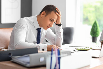 Fototapeta premium Tired male accountant working at desk in office