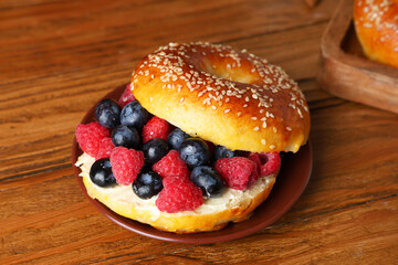 Plate of tasty bagel with butter and berries on wooden background