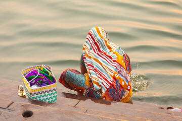 India, Uttar Pradesh, Varanasi. A woman in a colorful sari on the steps of a ghat washes in the...