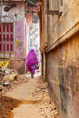 India, Uttar Pradesh, Varanasi. A woman in a purple sari walks down a rubble-strewn alley.