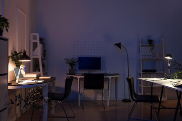 Interior of dark office with desks, plants and glowing lamps