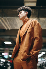 Stylish young man in an orange outfit standing confidently in a modern underground parking garage...