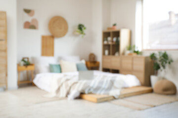 Blurred view of bedroom with laptop on big bed, drawers and plants