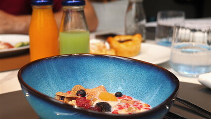 Close-up of nutritious breakfast with blue bowl of cereal topped with fruits and milk, accompanied by colorful juice bottles, on neatly set table. Healthy Eating and Nutrition.