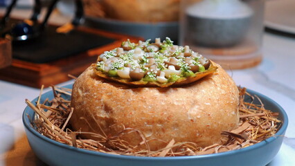 Gourmet dish featuring bread bowl filled with assorted vegetables and spices served creatively on blue plate, vibrant and appetizing presentation. Food Art and Culinary Creativity.