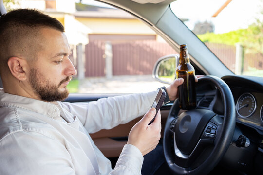 Man holding mobile phone and bottle of beer while driving car. Alcohol problem. Dangerous problem. Accident possibility