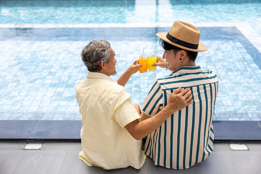 Asian father and son cheering on tropical fruit juice by the swimming pool in the hotel resort for summer travel vacation wellness and family, love, bonding concept - Powered by Adobe