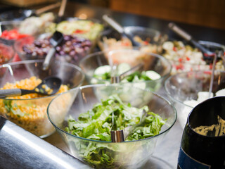 Various fresh vegetables in glass salad bowls with metal spoon, creating colorful and healthy display. Fresh vegetables offer vibrant nutrition and taste. Fresh vegetables in bowls ready to serve.