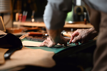 Close up view of craftsman skillfully using a cutting tool to shape the leather