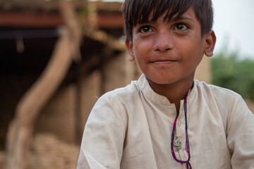 A young boy with dark hair and a serious expression, wearing a light shirt, sits outdoors