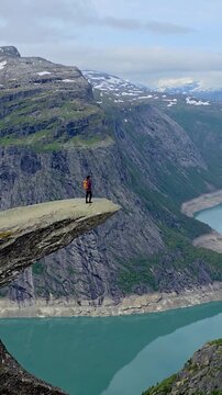 A dramatic scene featuring a women on a cliff near a stunning lake beneath a clear blue sky, blending modern elements with the beauty of nature, Trolltunga, Norway