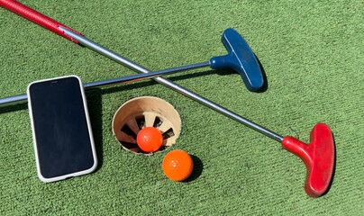 Series with golf clubs, smartphone and balls on artificial grass.