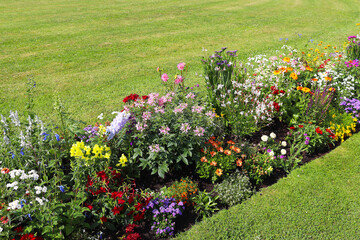 Green lawn framed by a garden bed of mixed summer flowers in various colors, Bavaria, Germany