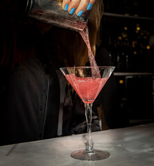 A cosmopolitan cocktail being poured by a bartender with blue fingernails at a bar