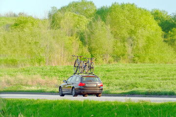 Fototapeta premium Family car with mountain bikes on roof rack driving on a sunny country road