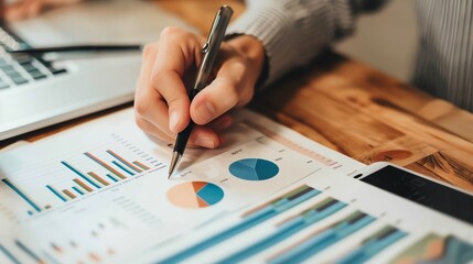 Close-up of a hand analyzing financial data with a pen and graphs.