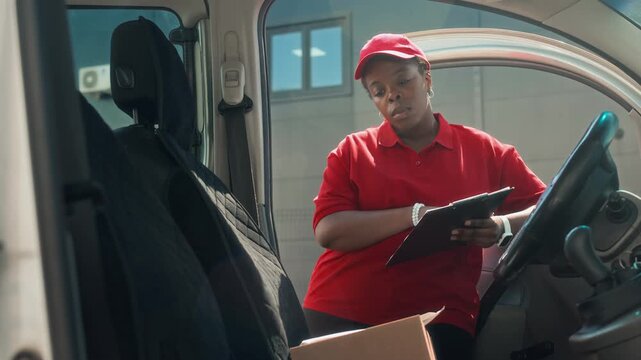 Handheld shot of African American woman taking cardboard box out of car when working at delivery service