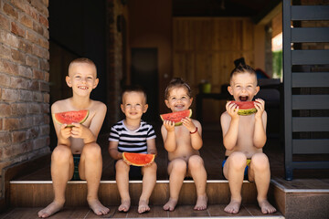 Happy kids sitting on a porch with watermelon slices in hands and smiling