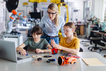 Female teacher helping to girls working on small robot, building robotic car in after-school...