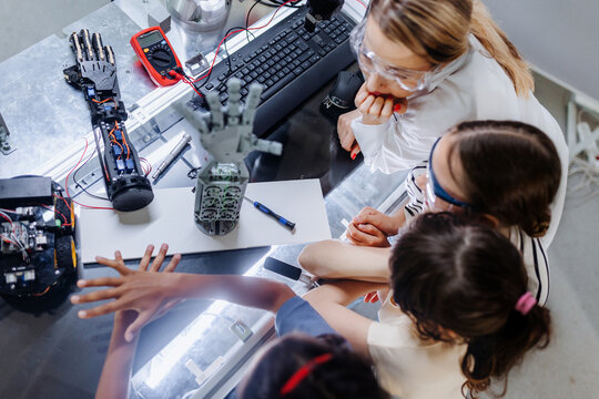 High angle view of teacher helping to girls working on small robot, building robotic kit in after-school robotics club. Children learning robotics in Elementary school. Girls in science.