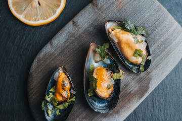 Mussels cooked in wine sauce with parsley, on a gray stone and a gray textured background.