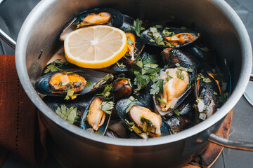 Mussels in white wine with parsley and lemon in a saucepan on a gray table. Close-up. Mediterranean cuisine, traditional French recipe.