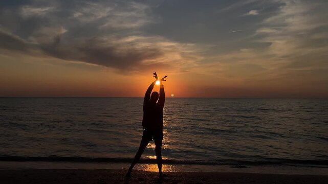 The silhouette of a girl dancing on the sand against the background of sunset and the horizon of the sea. 4k video. High quality 4k footage.