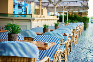Street cafe in morning. Empty outdoor patio with chairs and potted plants on table. Terrace with tables waiting for visitors in European city