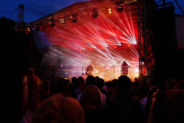 Silhouettes of crowd at concert in front of stage with bright spotlights. People enjoy live music at the band's performance. Concert hall with musicians on stage and fans during music festival