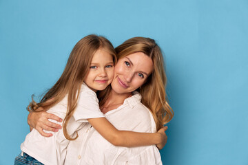 Smiling mother embracing her cheerful daughter against a vibrant blue background, capturing a...