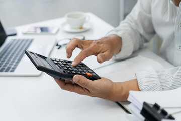 office employee works on desk, using calculator to manage financial documents and accounts,...