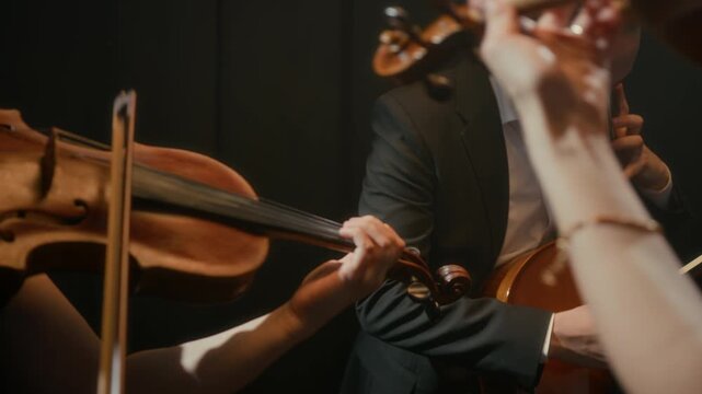 Aerial medium shot of professional string quartet in black outfits playing violins and cellos while giving concert on dark stage with cameras flashing