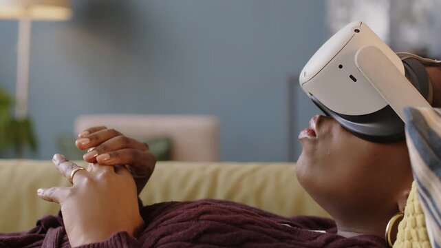 African American woman lying on her back on couch at modern therapist office wearing vr goggles and explaining her feelings during individual session with specialist