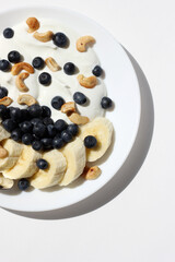 Greek Yogurt with Fresh Blueberries, Cashew Nuts, and Banana Slices on White Background. Healthy Breakfast.