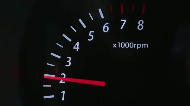 The video shows a close-up of a car tachometer with an arrow indicating revolutions per minute. The tachometer is black with white markings and a red arrow