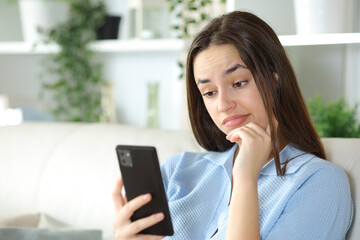 Disappointed woman checking cell phone at home