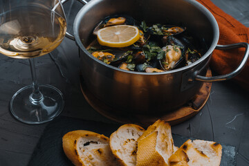 Mussels in wine with chopped parsley and lemon, a glass of white wine and a toasted baguette on a gray table. Traditional French and Italian dish
