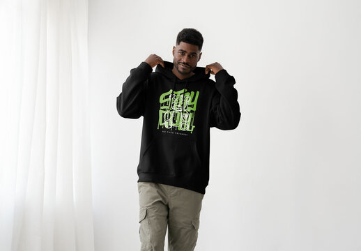 Mockup Of Cheerful Man In Studio Putting Hood Up On Customizable Hoodie