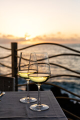 Romantic outdoor evening with two glasses of white wine and beautiful sunset on the sea beach at background. Italy, Sicily, evening time, summer. Vertical image.