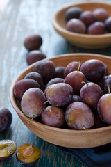 Fototapeta premium Ripe plum fruits on plate with water drops, on dark blue tablecloth and gray background. Aesthetic flat lay, closeup,