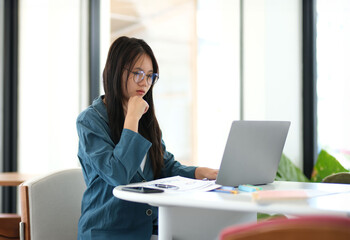Obraz premium A woman is sitting at a desk with a laptop open in front of her