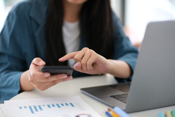 A woman is using a cell phone and laptop at a desk