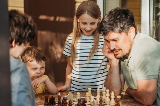 Happy family spending leisure time playing chess on porch