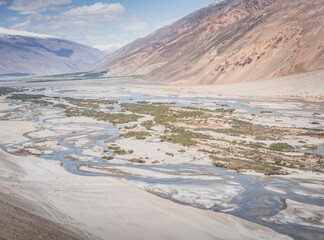 Pyanj River flows in Wakhan Valley among rocky high mountains against snow-capped peaks and glaciers in Tajikistan's Tien Shan mountains, landscape for background