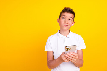 Photo of funny doubtful boy wear white t-shirt tying modern device looking emtpy space isolated...