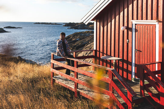 Thoughtful woman sitting on railing of porch at Lofoten and Vesteral Islands